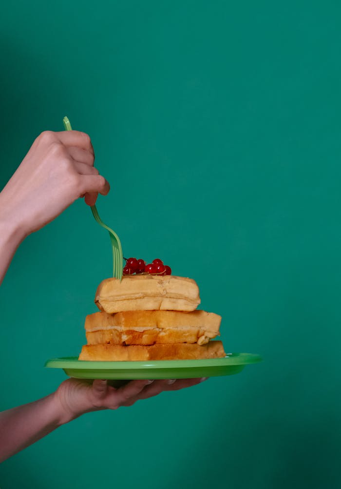 Close-up of waffles on a green plate with berries, held by a hand.
