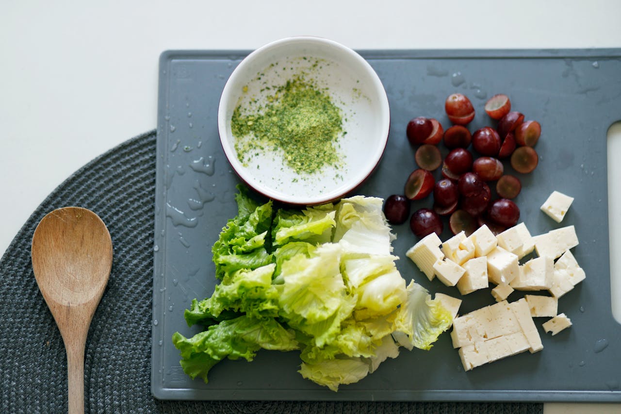 who-we-are Fresh lettuce, grapes, and tofu with seasoning on a cutting board for a healthy meal preparation.