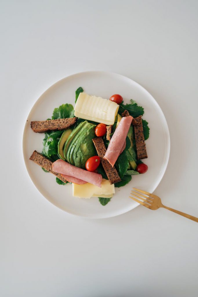 Fresh salad plate with avocado, ham, rye bread, and cheese slices, perfect for a healthy start.