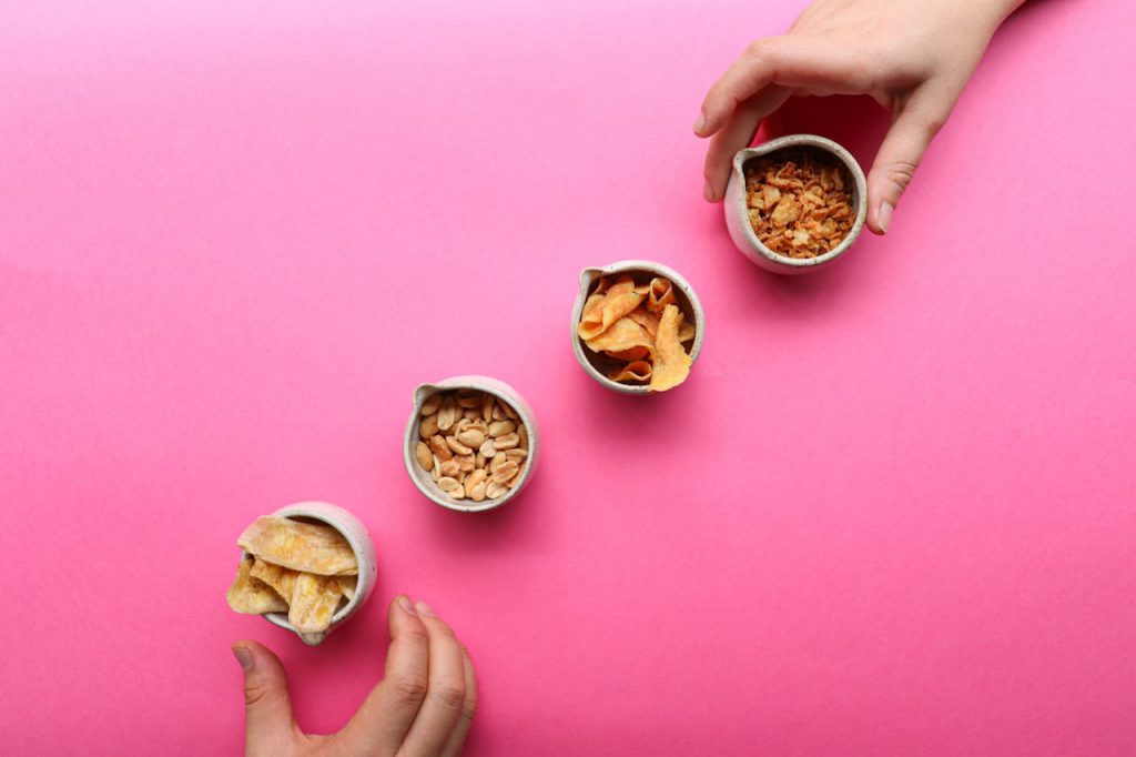 Colorful display of various healthy snacks in bowls on a pink backdrop, ideal for health and lifestyle themes.